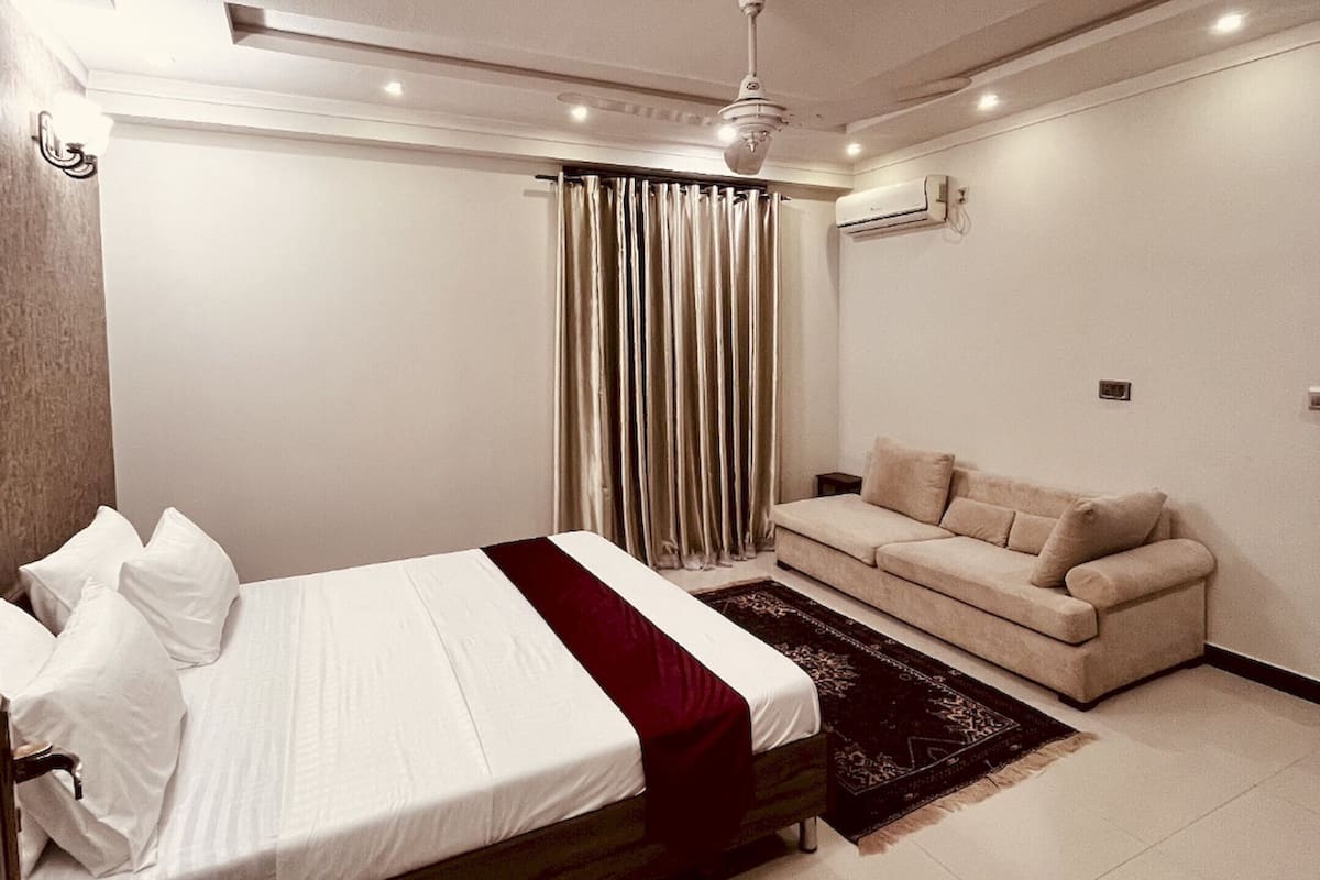 Un dormitorio moderno con cama, sofá, ventilador de techo y aire acondicionado.