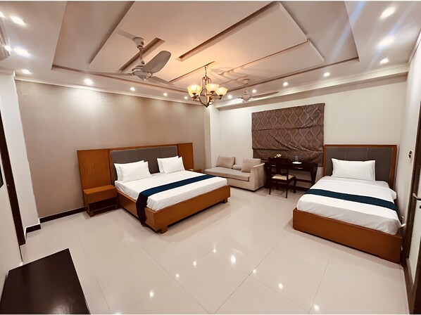 A hotel room with two beds, a sofa, a desk, a chandelier, and a ceiling fan. - AlYasir lodges (Islamabad)