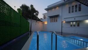 A swimming pool with metal railings, surrounded by a white building with windows and a balcony. - Cool Nest Pool Villa Munnar by VOYEHOMES (Devikolam)