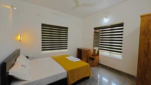 A bedroom with a bed, two windows with blinds, a ceiling fan, and a wooden wardrobe. - Cool Nest Pool Villa Munnar by VOYEHOMES (Devikolam)
