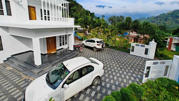 A modern two-story house with a carport, a white car, and a motorcycle parked in front. - Cool Nest Pool Villa Munnar by VOYEHOMES (Devikolam)