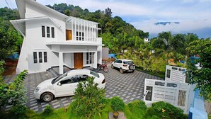 A modern two-story house with a car parked in the driveway and a motorcycle in the background. - Cool Nest Pool Villa Munnar by VOYEHOMES (Devikolam)