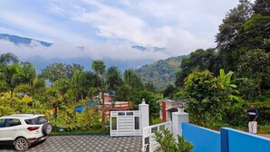 A gated entrance with a paved driveway, surrounded by lush greenery and a mountainous backdrop. - Cool Nest Pool Villa Munnar by VOYEHOMES (Devikolam)