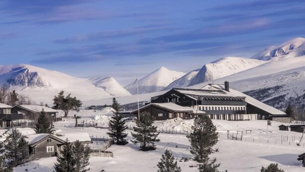 A snow-covered mountain resort with cabins and a large building, likely a lodge or restaurant, surrounded by snow-covered peaks. - Rondablikk (Nord-Fron)