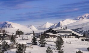 A snow-covered mountain resort with cabins and a large building, likely a lodge or restaurant, surrounded by snow-covered peaks.