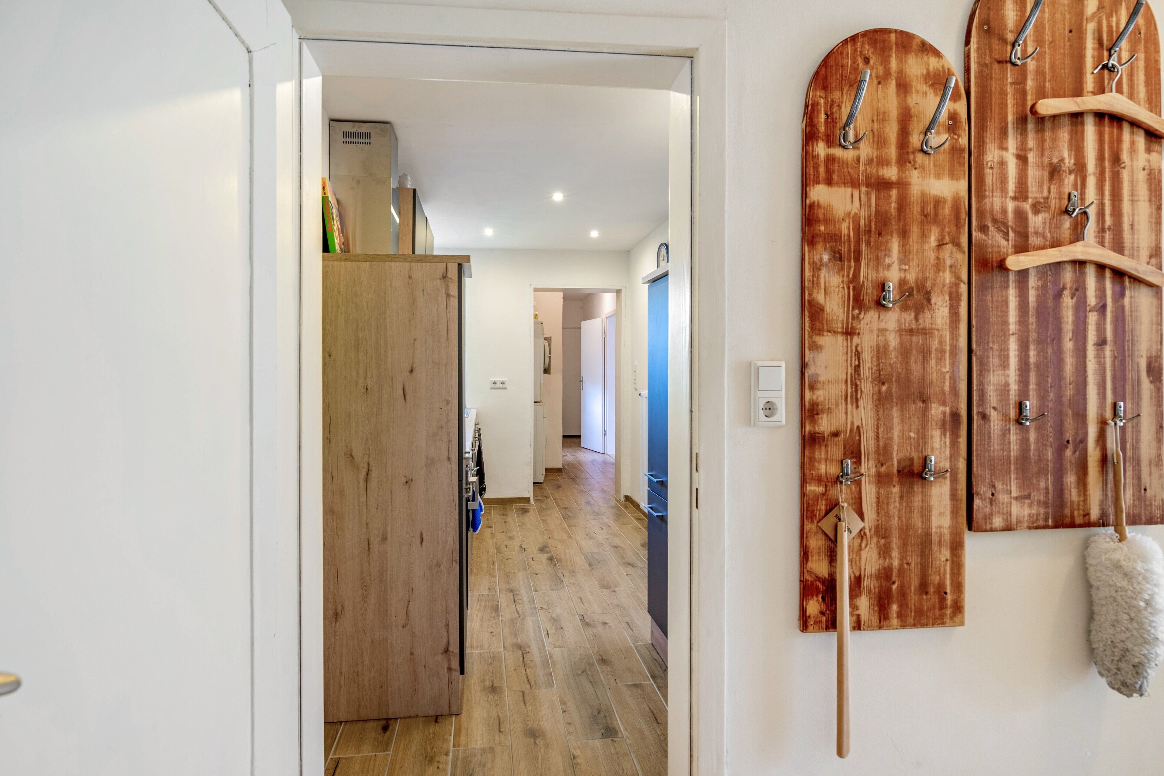 Een gang met houten vloer, een houten deur en een kapstok aan de muur met hangers.