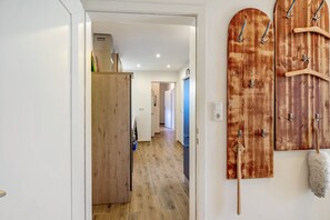 A hallway with wooden flooring, a wooden door, and a wall-mounted coat rack with hangers. - Ground Floor Apartment (Lichtenau)