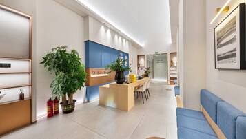 A modern hotel lobby with a reception desk, seating area, and a large potted plant.