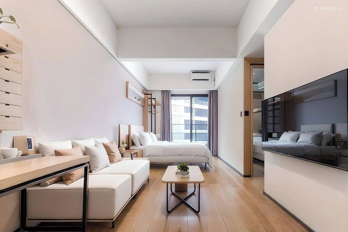 A modern hotel room with a sofa, a small table, a bed, a TV, and a window with curtains.