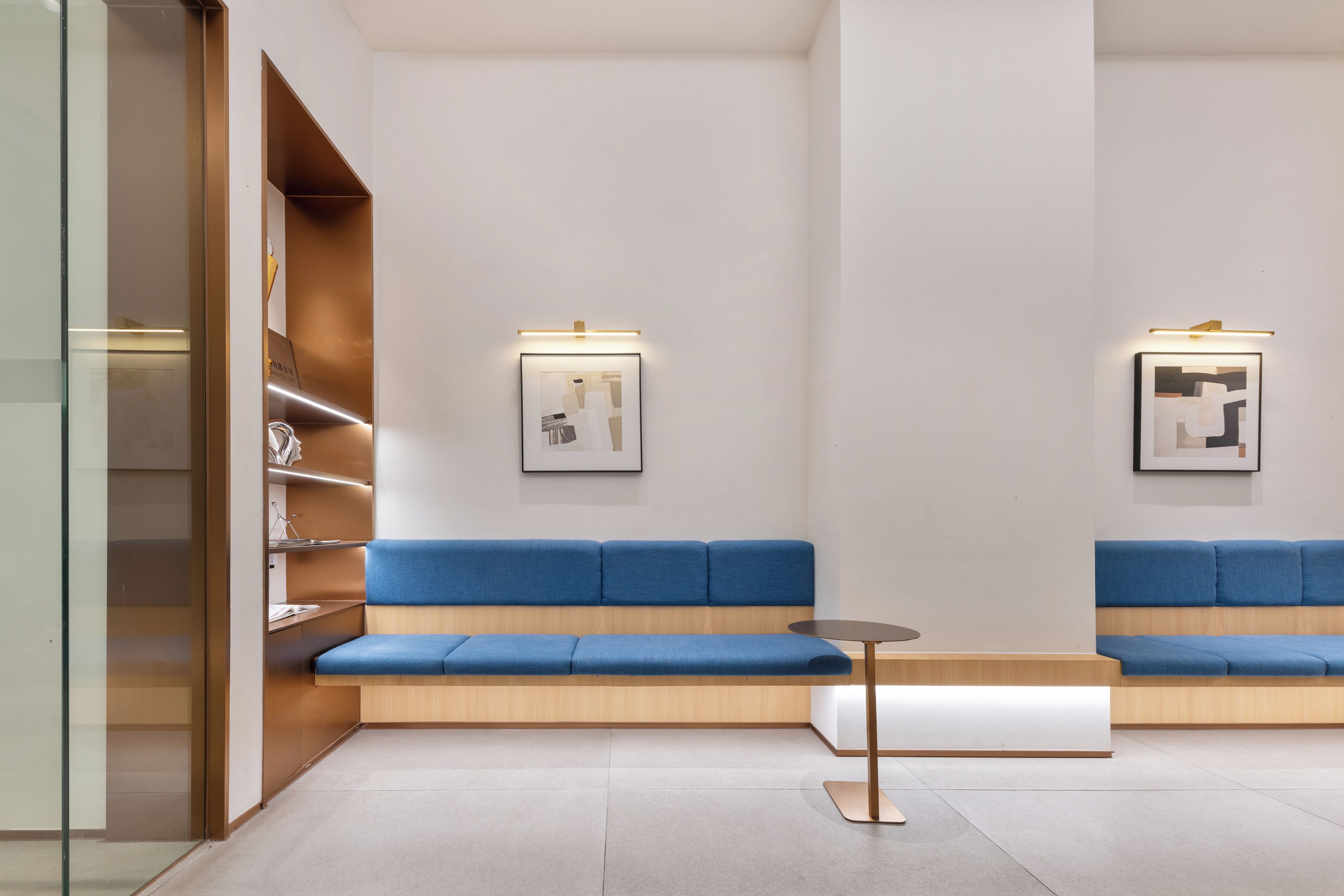 A modern waiting area with blue cushioned seating, a small table, and framed artwork on the walls.