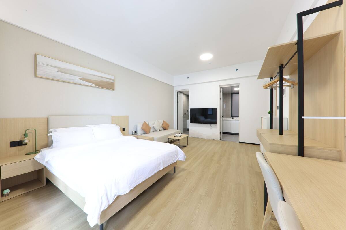 A modern hotel room with a large bed, a desk, a sofa, and a TV.