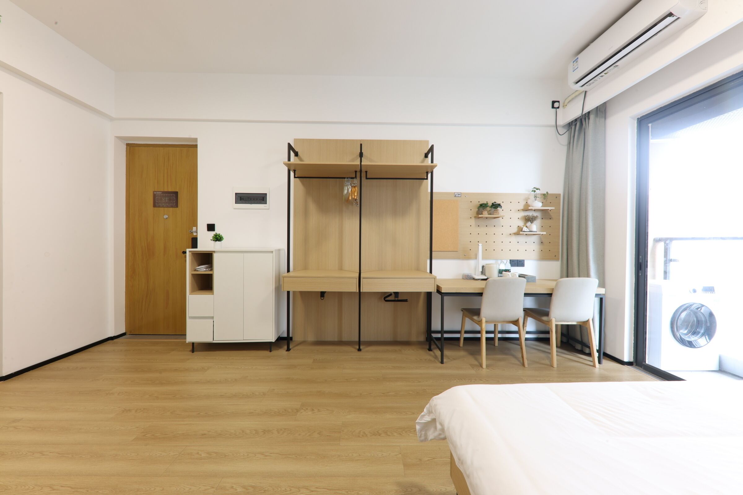 A hotel room with a bed, a desk, a chair, a wardrobe, and a washing machine.