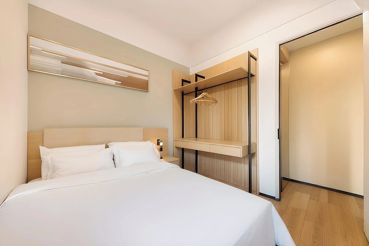 Een moderne hotelkamer met een bed, een aan de muur bevestigde televisie, een houten garderobe en een kapstok.