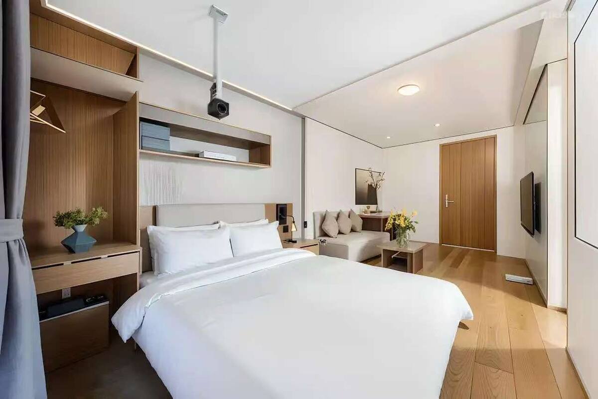 A modern hotel room with a large bed, a desk with a computer, a sofa, a TV, and a wardrobe.