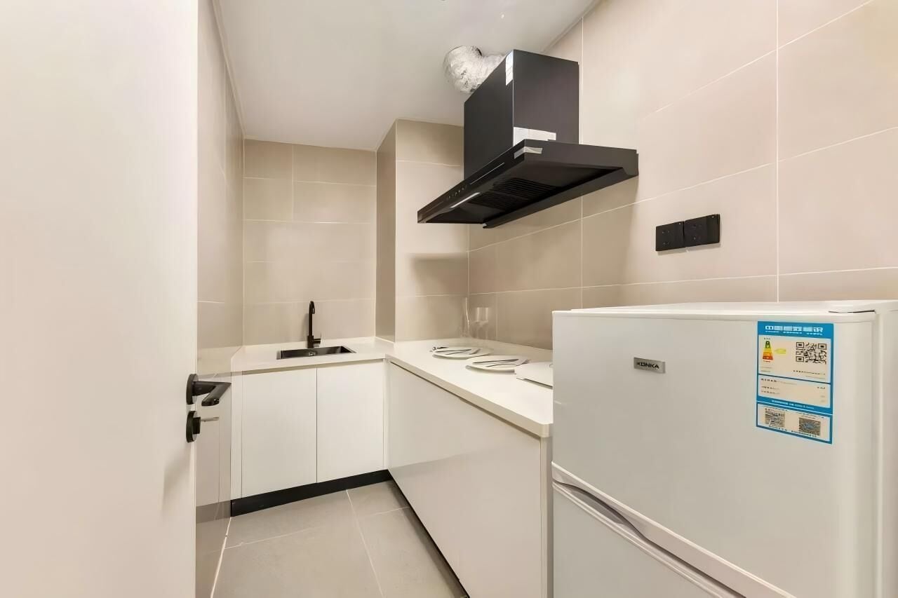 A modern kitchen with white cabinets, a black range hood, and a white refrigerator.
