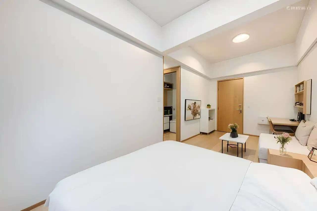A modern hotel room with a large bed, a desk, a chair, and a small table with a vase.
