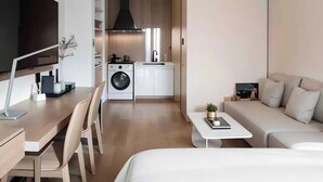 Una habitación de hotel moderna con cama, escritorio, sofá, televisor, lavadora y kitchenette.