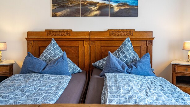 Un lit double avec une couvre-lit à motifs, deux oreillers assortis, une tête de lit en bois et une œuvre d’art fixée au mur représentant une scène de plage.