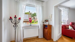 Une pièce avec une fenêtre, un canapé rouge, un meuble en bois et un chandelier avec des bougies.