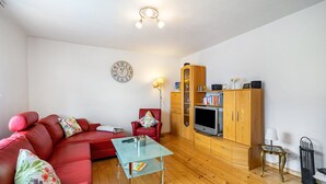 Un salon avec un canapé rouge, une table basse en verre, des meubles en bois, un téléviseur et une horloge au mur.