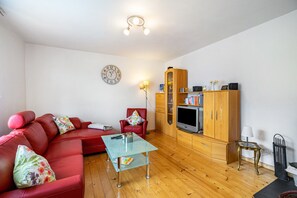 A living room with a red sofa, a glass coffee table, wooden cabinets, a television, and a clock on the wall. - Upstairs Apartment in Husen’s Altenautal, Near Paderborn (Lichtenau)