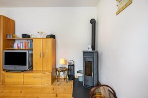 A living room with a TV, wooden cabinets, a bookshelf, a lamp, a chair, a fireplace, and a trash can. - Upstairs Apartment in Husen’s Altenautal, Near Paderborn (Lichtenau)
