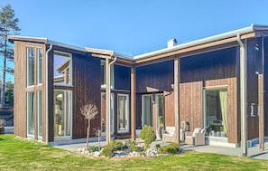 A modern house with large glass windows, a wooden exterior, and a well-maintained garden.