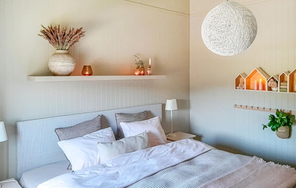 A bedroom with a bed, bedside tables, a lamp, a hanging light fixture, and decorative shelves.