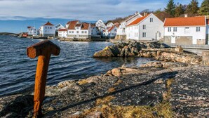 Rannikkokaupunki, jossa on valkoisia rakennuksia ja punaisia kattoja, kivikkoinen rantaviiva ja vasara etualalla.