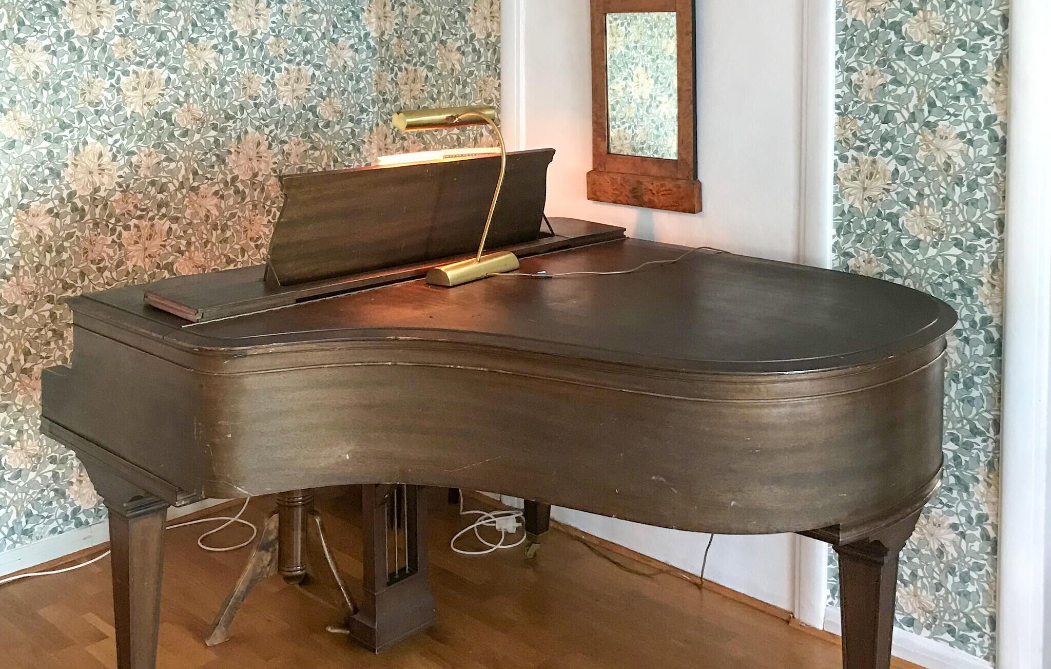 A grand piano in a room with patterned wallpaper and a mirror on the wall.