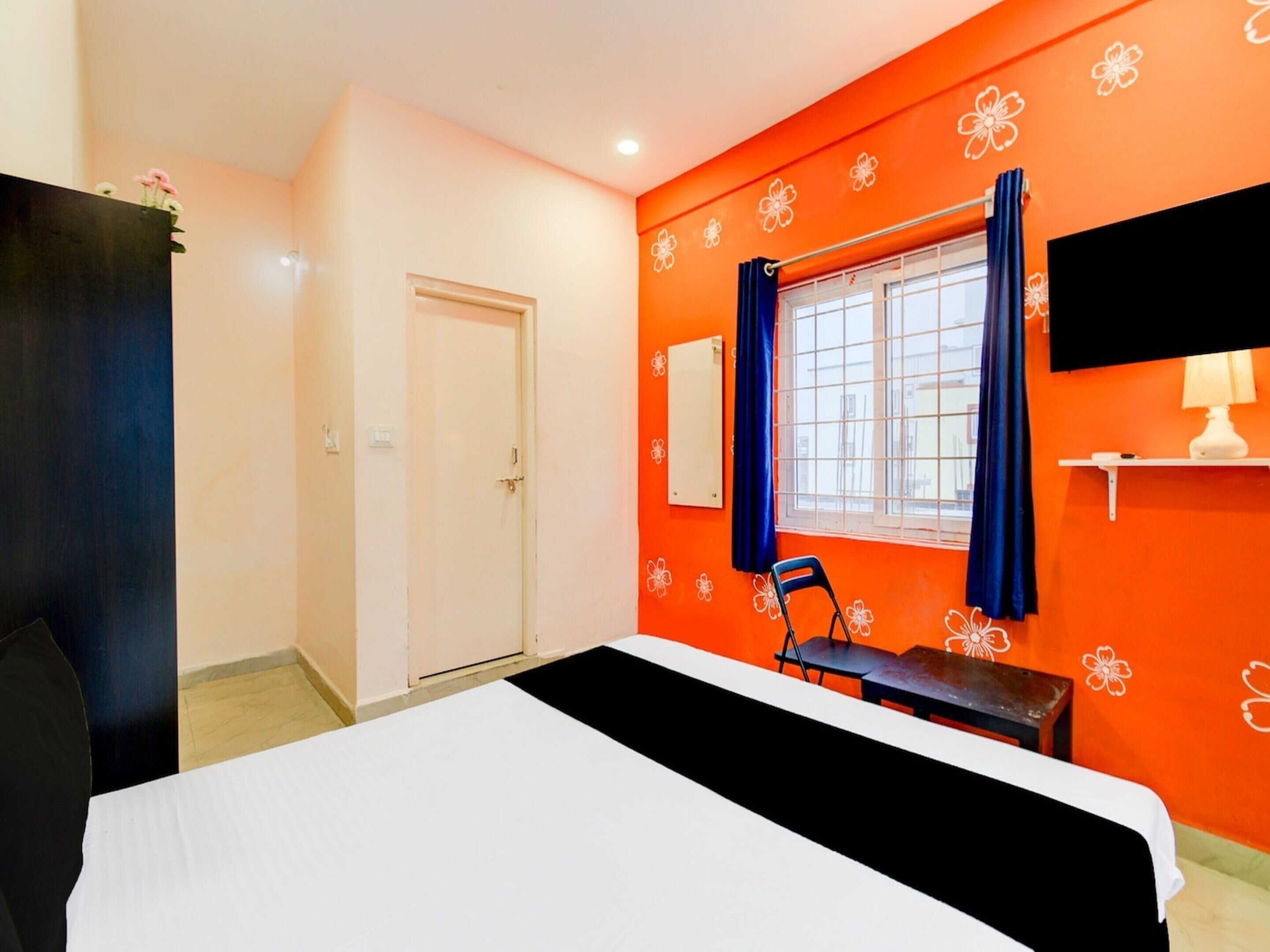 Een kamer met een bed, een stoel, een raam met gordijnen, een televisie en een bloemenpatroon op de muur.
