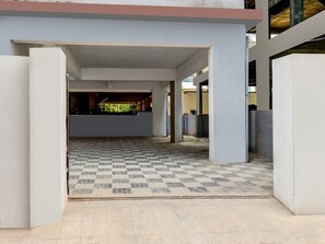 Un área de estacionamiento techada con un piso de patrón cuadriculado, pilares de concreto y vista a un edificio con techo verde.