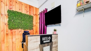 A reception desk with a 'HOTEL' sign, a wooden wall with a green wall-mounted plant, a black curtain, and a mounted TV. - Deluxe Hotel Nakshatra (Patancheruvu)