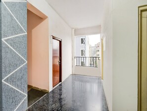 Un pasillo con piso de mármol, una puerta de madera y un balcón con barandilla de metal.