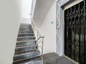 Una escalera con barandillas de metal que lleva a una puerta con una celosía metálica geométrica.