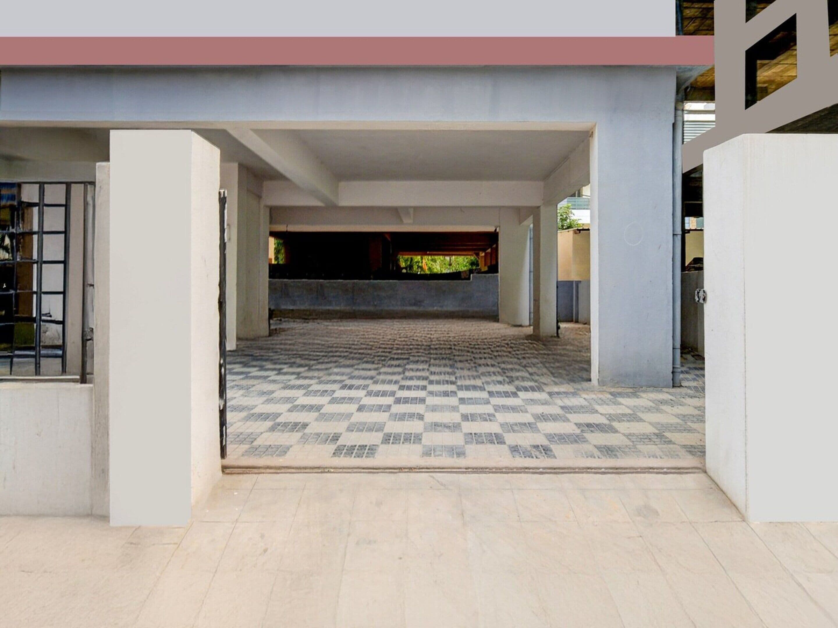 A covered outdoor area with a checkered floor, concrete pillars, and a view of a building in the background.