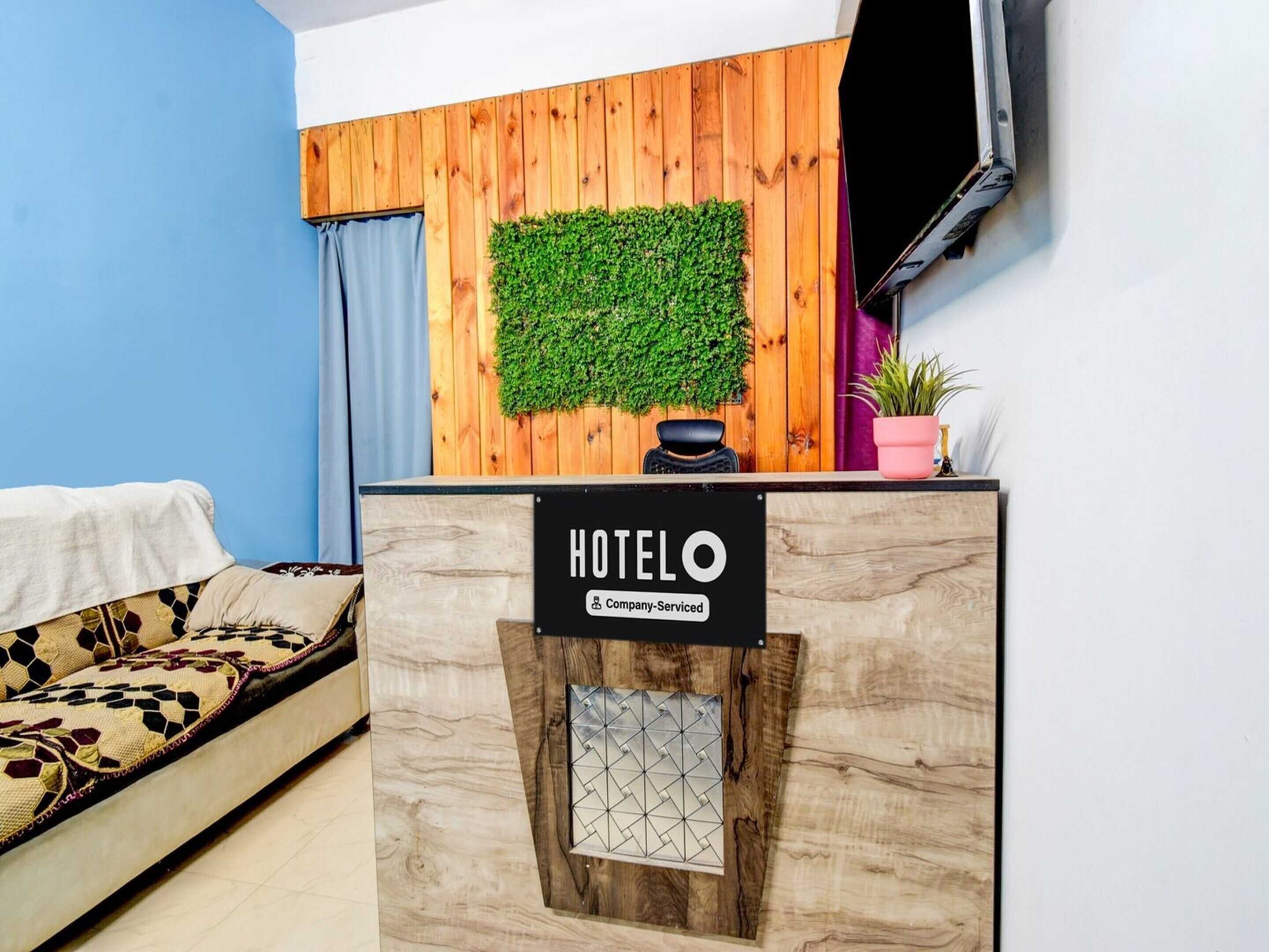 Un mostrador de recepción de hotel con un panel de pared de madera, una planta verde y un cartel que indica que es un hotel con servicios para empresas.