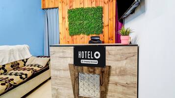 Un mostrador de recepción de hotel con un panel de pared de madera, una planta verde y un cartel que indica que es un hotel con servicios para empresas.