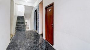 A hallway with a marble floor, a wooden door, and a staircase leading to another room. - Deluxe Hotel Nakshatra (Patancheruvu)