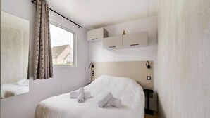 Une chambre à coucher comprenant un lit, une fenêtre avec des rideaux, un miroir, une table de chevet et un luminaire fixé au mur.