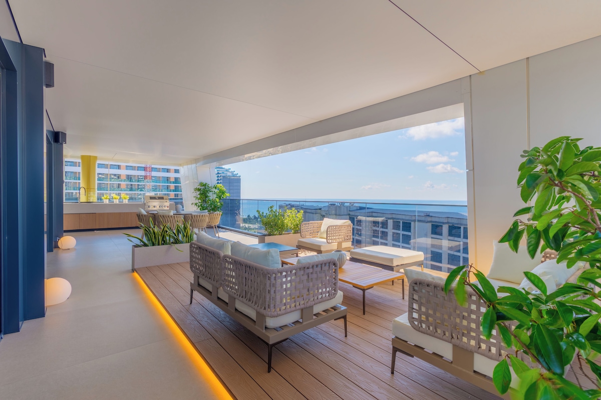 A modern living room with a balcony, furnished with sofas and a coffee table, overlooking a cityscape.