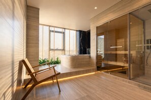 A modern bathroom with a glass shower enclosure, a wooden bench, and a seating area with plants.