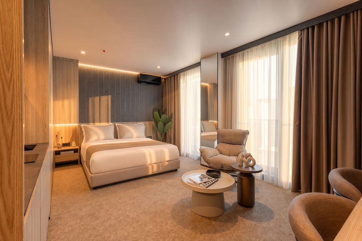 Una habitación de hotel moderna con una cama grande, un área de descanso con una mesa de centro, una mesita auxiliar y una silla.