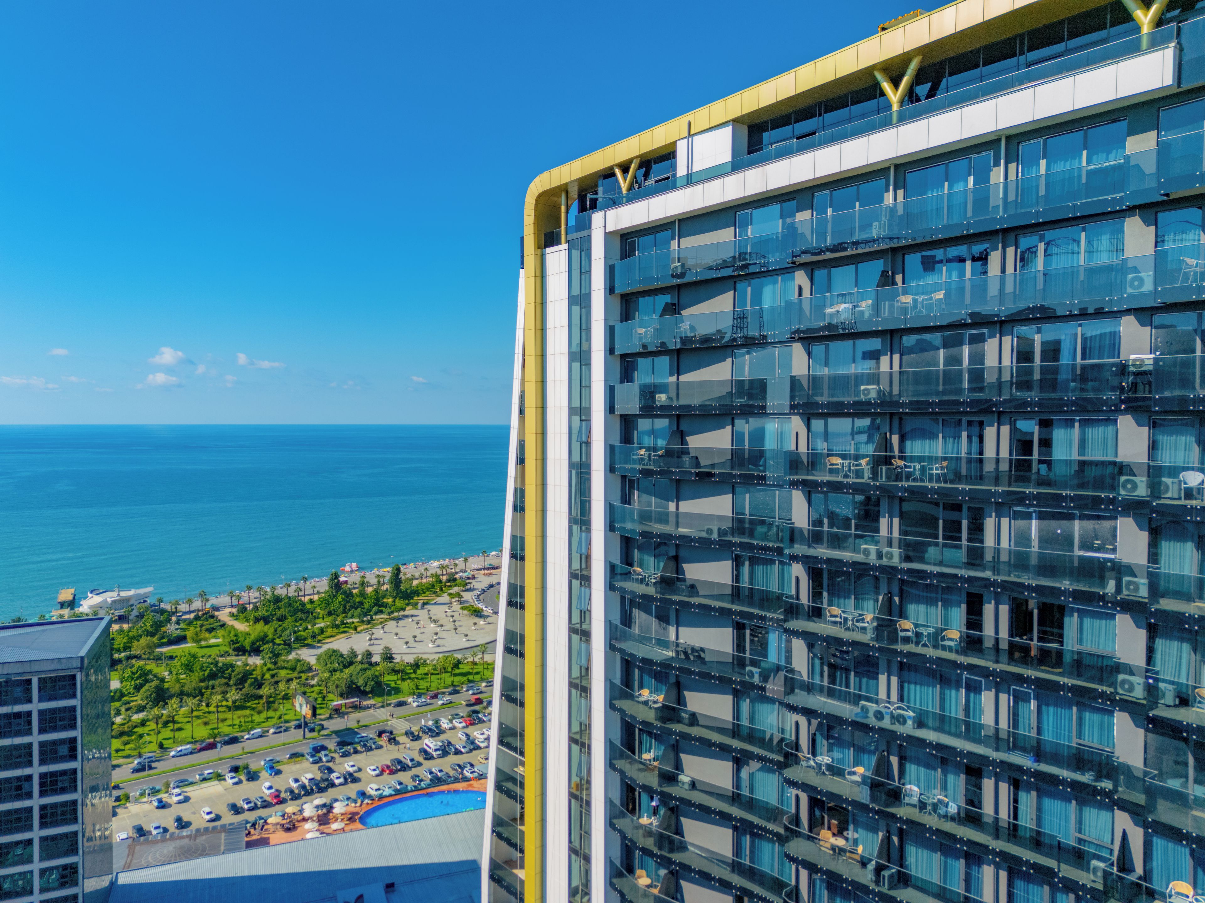 A high-rise hotel with multiple balconies, a pool area, and a view of the ocean.