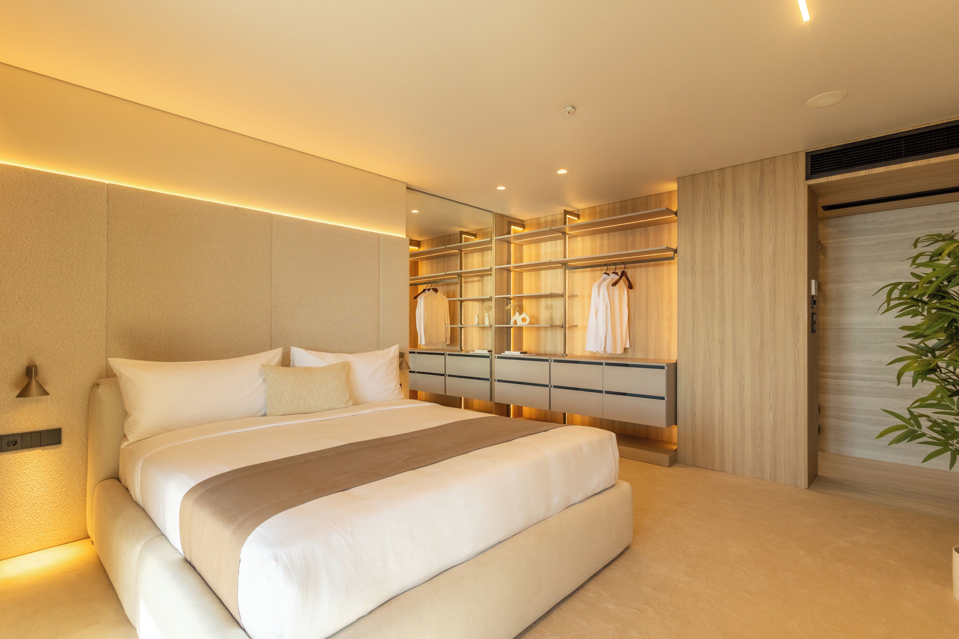 A modern bedroom with a large bed, built-in wardrobe, and a mirror.