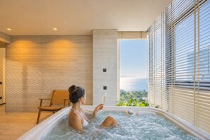 Une femme dans un bain à remous, un verre de vin à la main, entourée de murs en bois, avec une vue sur la verdure.