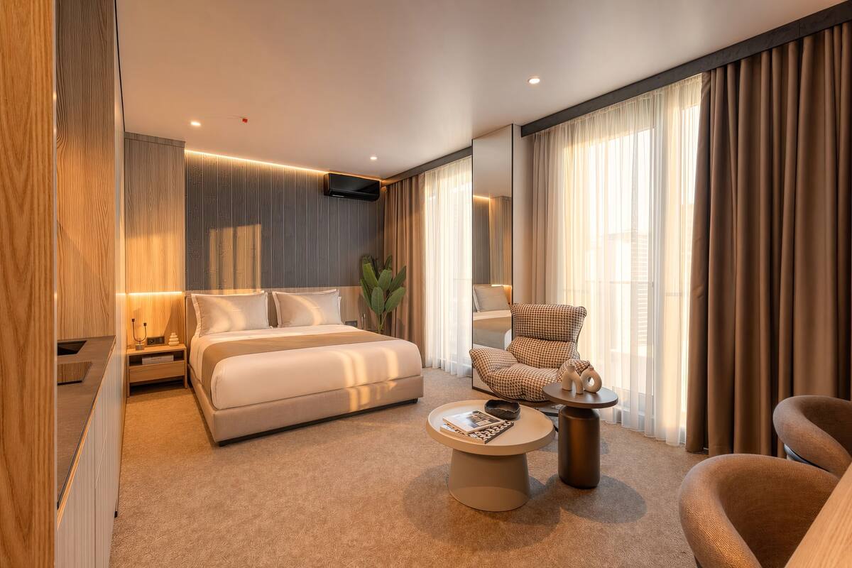 Una habitación de hotel moderna con una cama grande, un área de descanso con una mesa de centro, una mesita auxiliar y una silla.