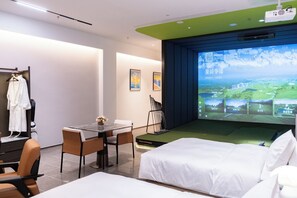 Quarto de hotel com cama, escrivaninha e cadeira, TV exibindo uma paisagem, e um cabideiro com roupão.