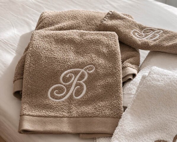 Ein ordentlich gefaltetes, beige Handtuch mit einem Monogramm auf einem Bett.