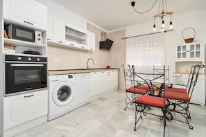 Eine moderne Küche mit Waschmaschine, Backofen, Mikrowelle und einem Essbereich mit Tisch und Stühlen.